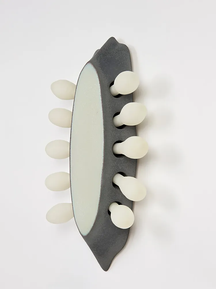 Vue en perspective de l’applique en grès émaillé gris entourée d’éléments en verre dépoli