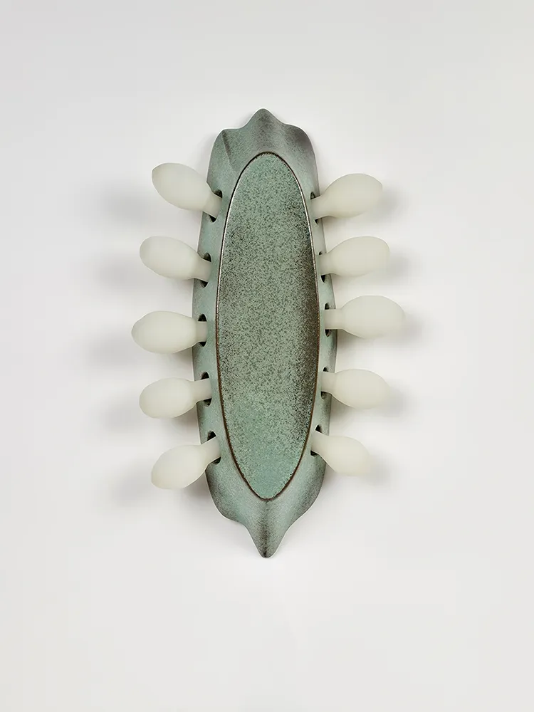 Vue de face de l’applique en grès émaillé vert entourée de dix éléments en verre dépoli
